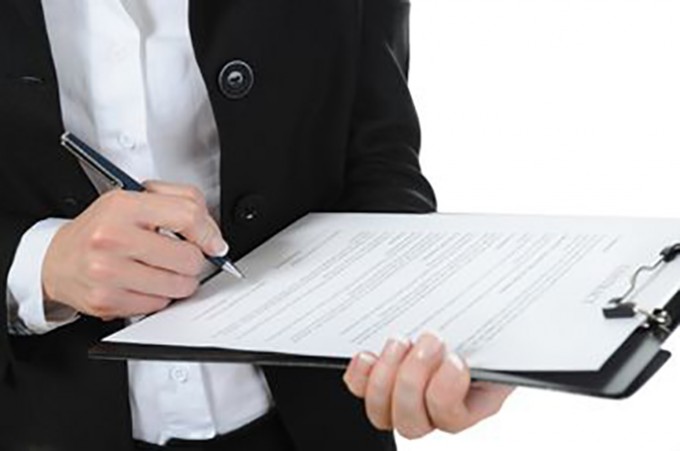 Woman is writing with a pen on the clipboard that she is holding