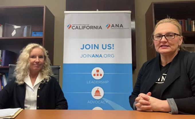 Two nurses in business attire are sitting and smiling in front of a sign for the California ANA Organization