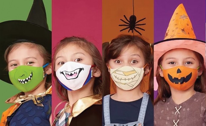 Four girls are smiling with different monster masks. Each one is in front of a different background color and with a different costume on.