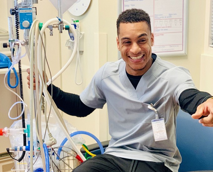 Registered Nurse Roosevelt Davis in scrubs is smiling while holding a piece of equipment