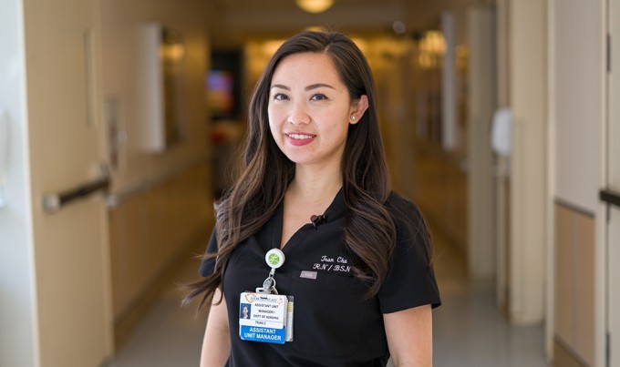 Tran Chu wearing scrubs and smiling while standing in front of a hallway