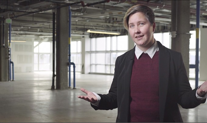 Woman is standing in an empty warehouse talking to the camera