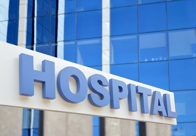 Blue "Hospital" sign on a white building with another blue building behind it