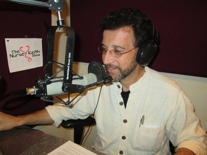 Nurse Keith Carlson sits next to his recording equipment with a sign for "The Nurse Keith Show" in the background