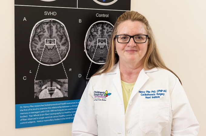 Registered Nurse Nancy Pike smiles in a white coat, standing in front of brain imaging.