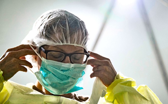 Nurse is removing a mask while wearing an isolation gown and head cover