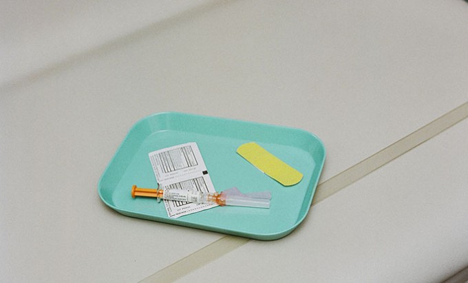 A green tray sits on a counter with a syringe, barcode stickers, and a yellow bandaid