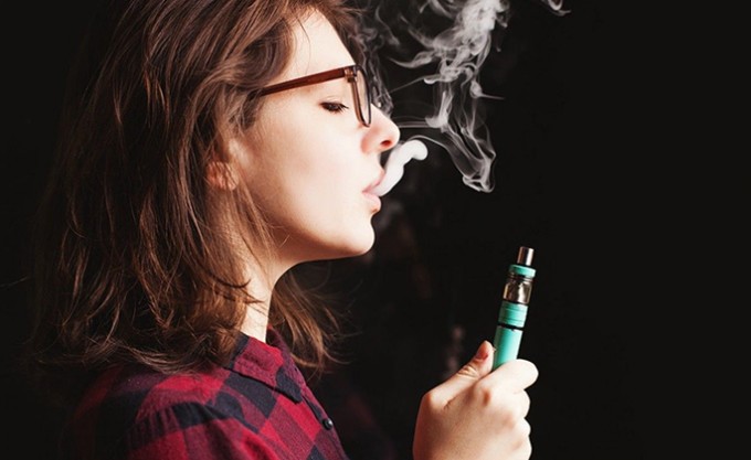 Woman breathes out smoke while holding a vape pen