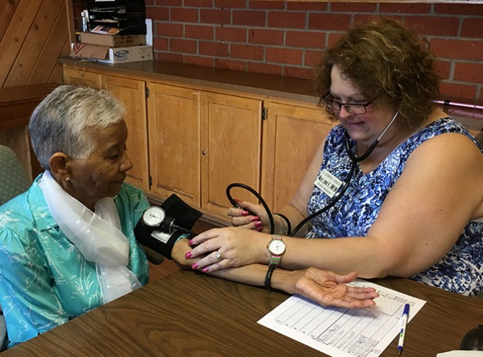 A nurse is taking the blood pressure of an older patient while they both sit at a table