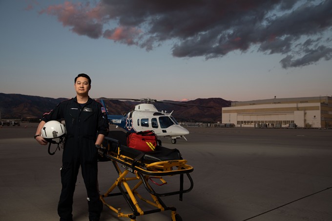 Andrew Tran wearing flight nursing uniform stands next to a gurney in front of a helicopter