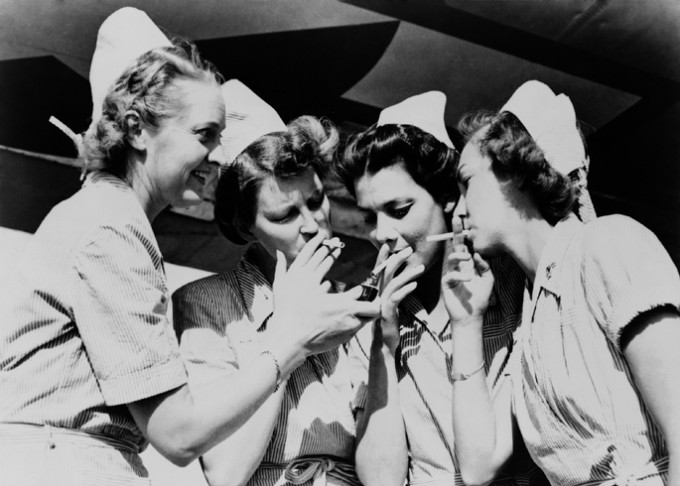 A group of female nurses in dresses and caps are smoking together