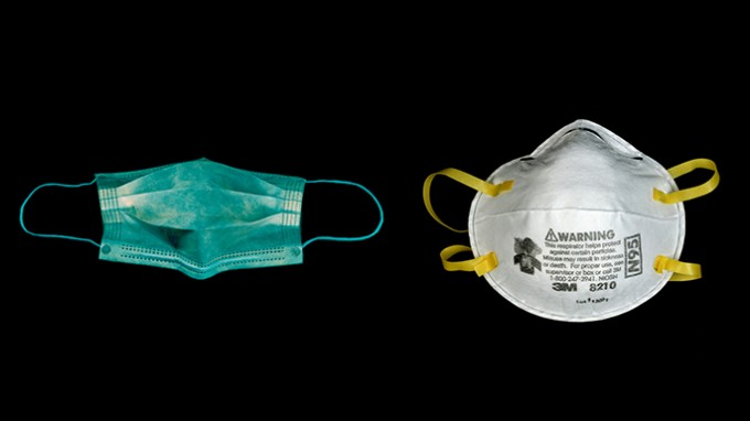 A surgical mask and N-95 mask lay next to each other on a black background