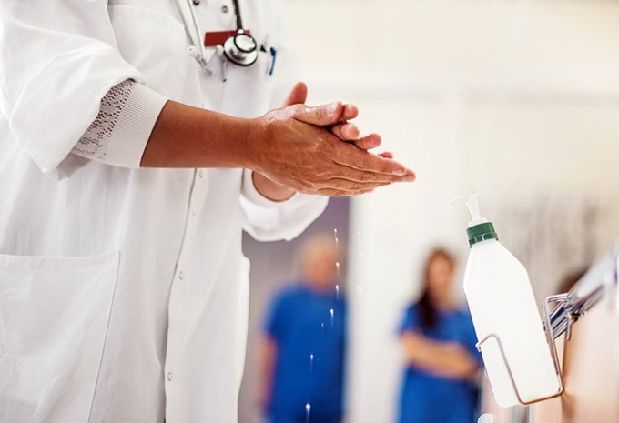 Nurse in white coat and stethoscope around their neck is scrubbing their hands