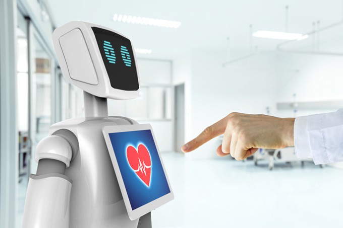 A nurse is clicking on a robots screen which shows a heart and EKG