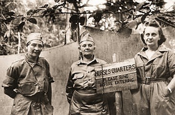 Three nurses in military uniforms stand around a sign that states "Nurses Quarters"