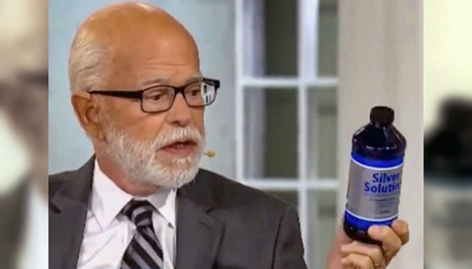 Newscaster holding a blue bottle of colloidal silver and reading the label