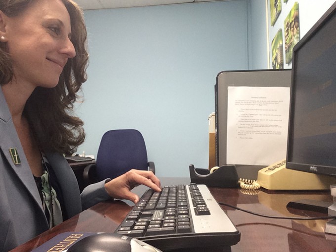 A nurse in business attire is smiling at the computer she is typing on