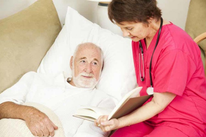 Nurse in pink scrubs is reading to her patient who is in a bed