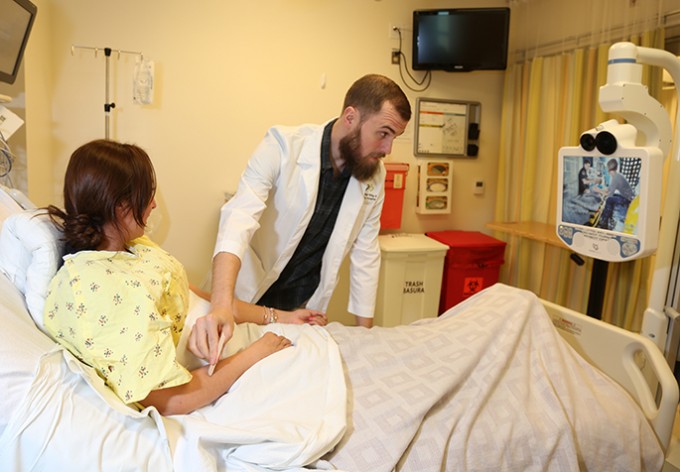 A nurse in a white coat is taking an ultrasound of a patient lying on a hospital bed