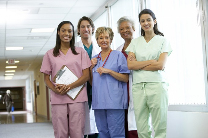 Five nurses in different scrubs stand next to each other smiling