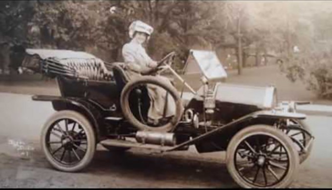 Katherine Buckner Avery sits in an old car with a gown and hat on
