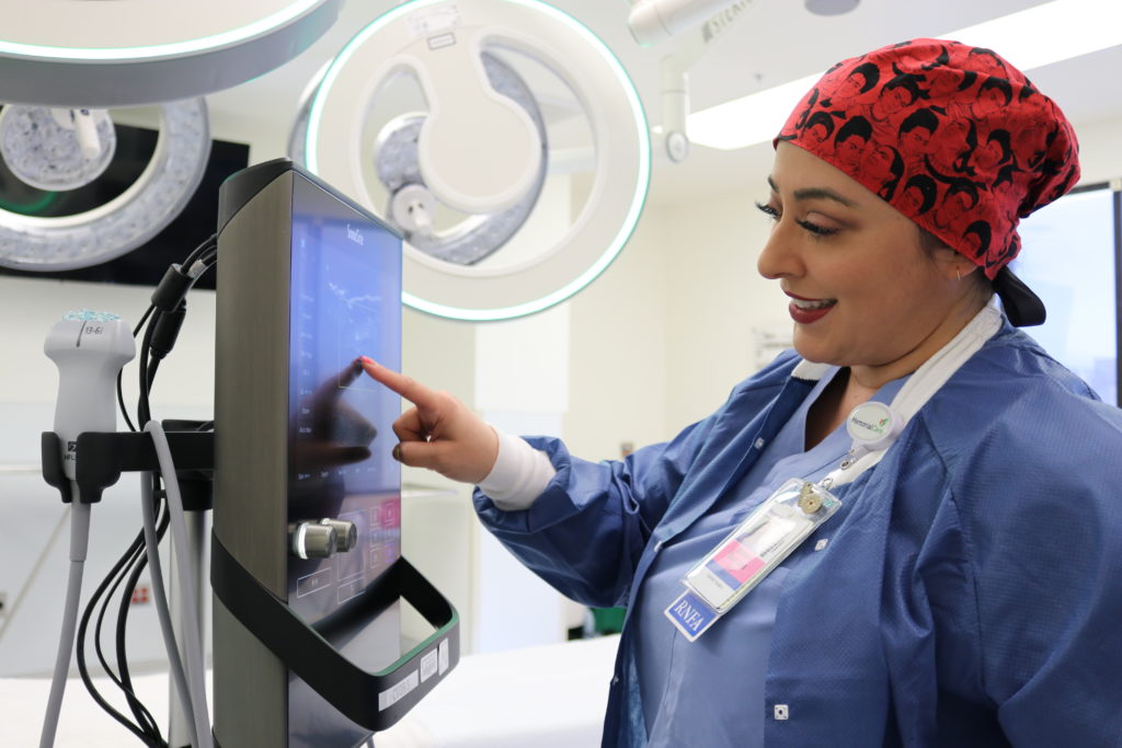 Bobbie Barraza wearing scrubs stands in front of a computer in the operating room