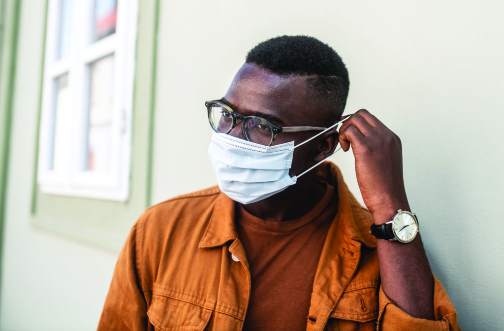 A young black man stands alone on the street and puts a mask on his face