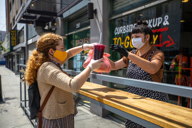 Woman being handed a drink by another woman at a to-go restaurant