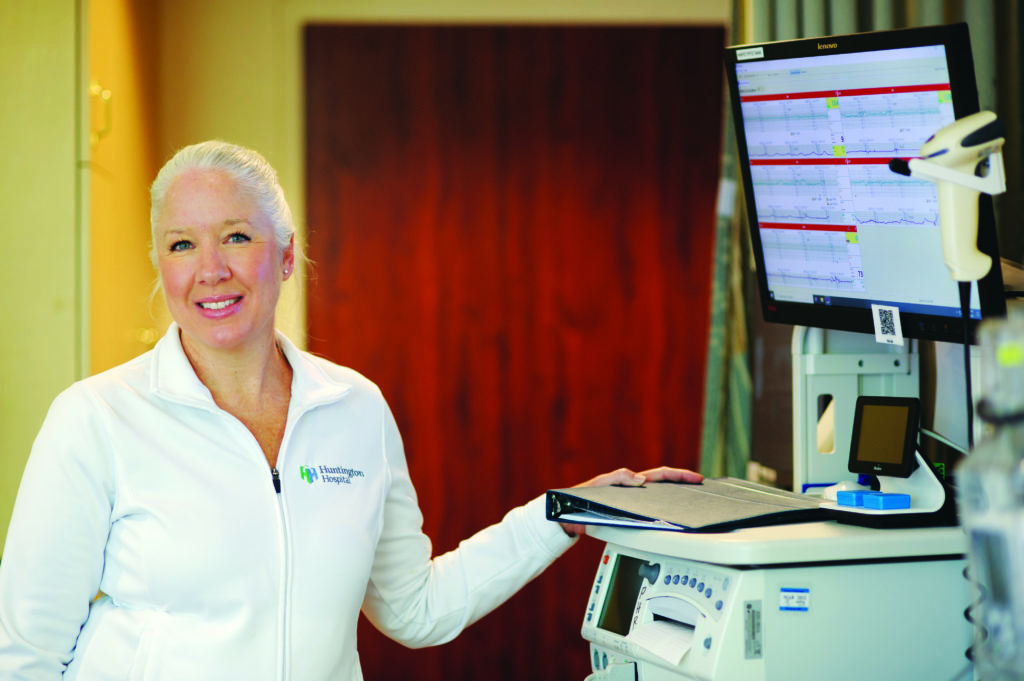 Terri Smith in a white coat stands smiling in front a computer