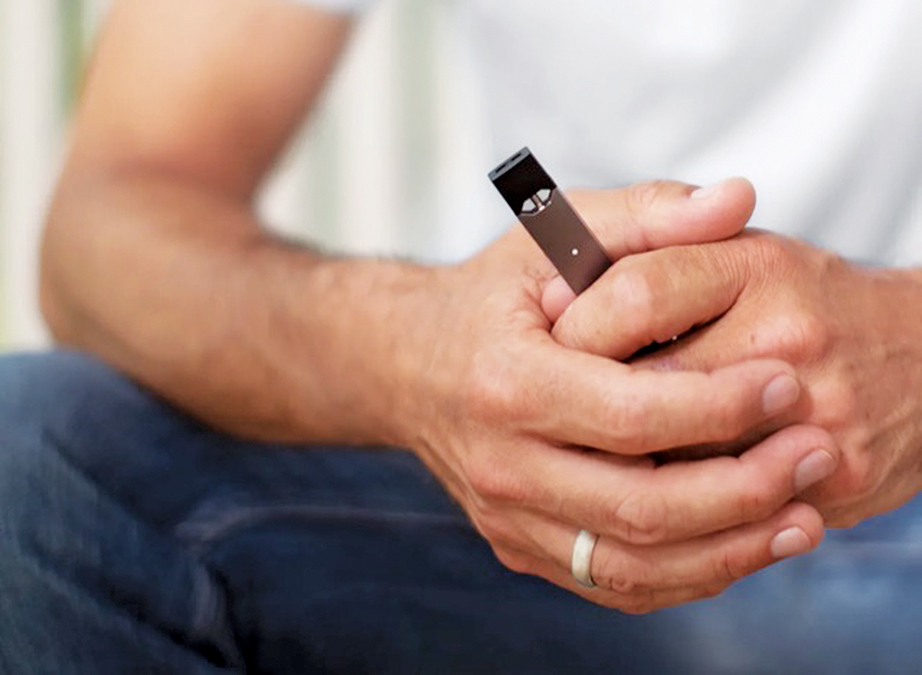 Man is sitting down and holding a JUUL in his clasped hands