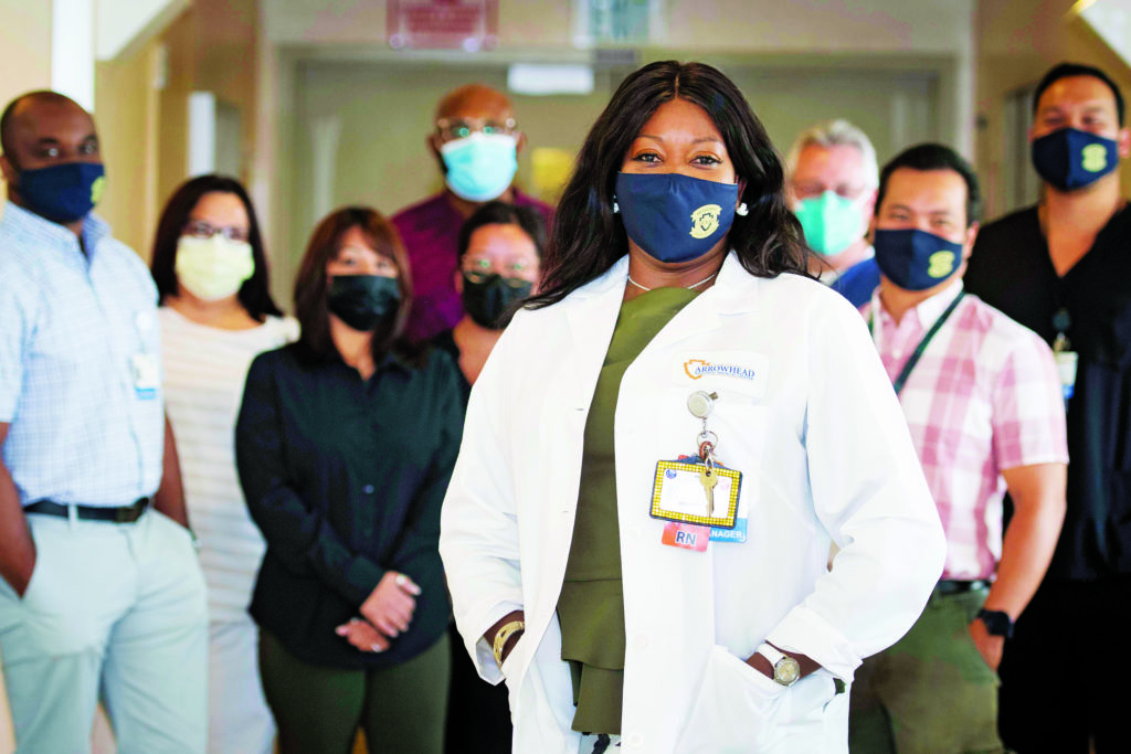 Sandy Kesler-Newman wearing a white coat and mask stands in front of nursing staff.