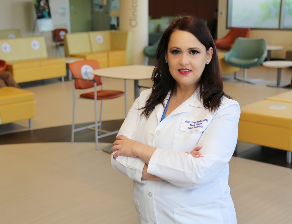 Martha Lopez wearing a white coat is smiling while sitting with arms crossed