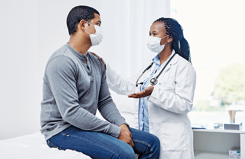 Nurse practitioner is talking to her patient who is sitting on a patient table in front of her. She is touching his arm.