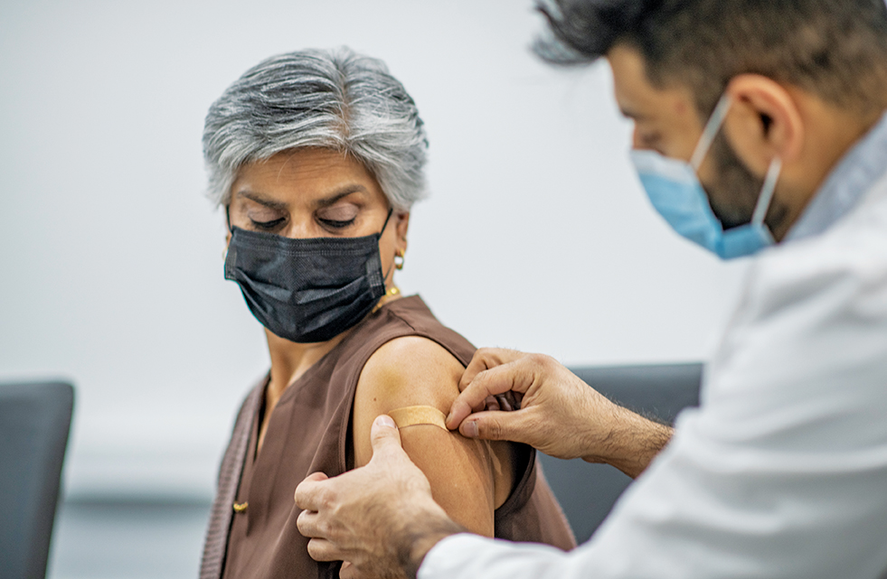 Doctor placing a bandaid on a patient's left arm after she is given a vaccine