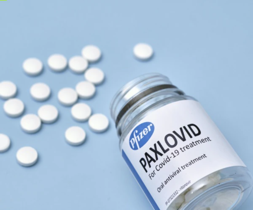 Paxlovid bottle lays on a blue counter and pills are scattered around.