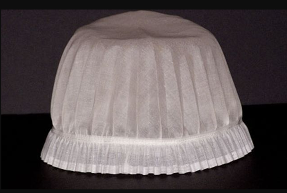 White nursing cap with frills on the base, lays on top of a black counter