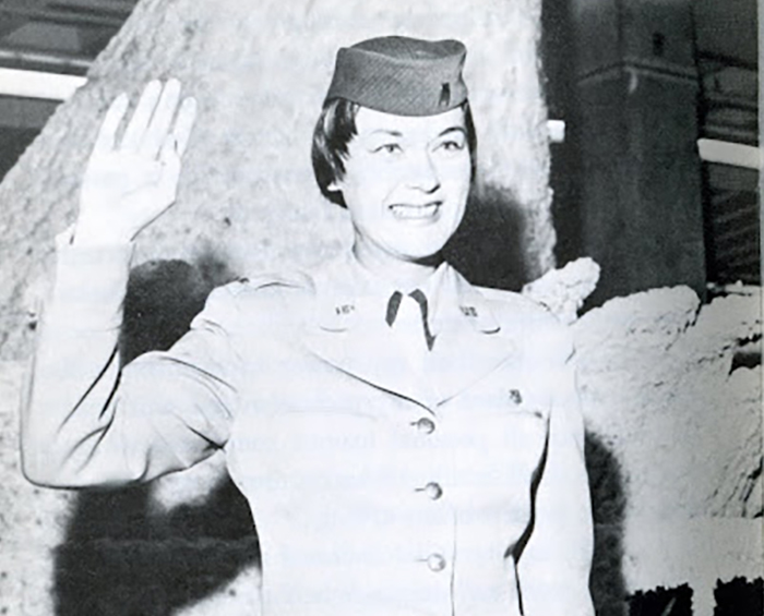 Dolores O'Hara in uniform and smiling while holding her right hand up waving