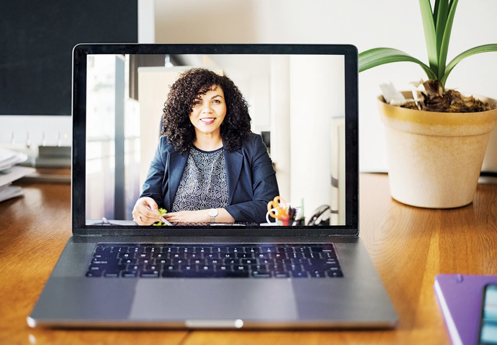 A woman is smiling at us in business casual clothes on the monitor of the computer