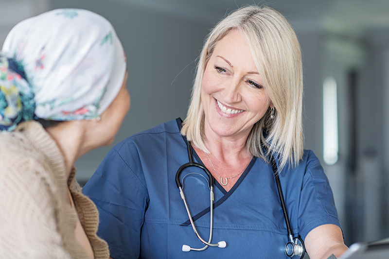 Nurse practitioner in blue scrubs and with a stethoscope around her neck is smiling at her patient