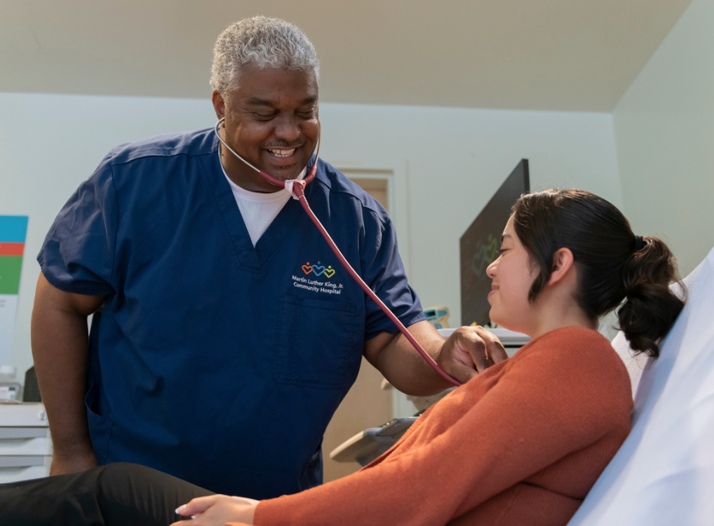 Jesse Lynwood wearing scrubs and listening with stethoscope to a patient's heart