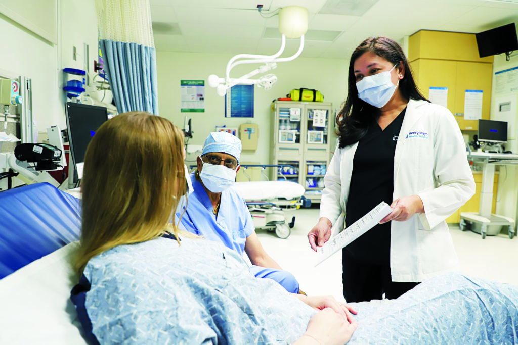 Patient lying down in bed, while a nurse is standing in a white coat and holding paperwork for the patient to look at