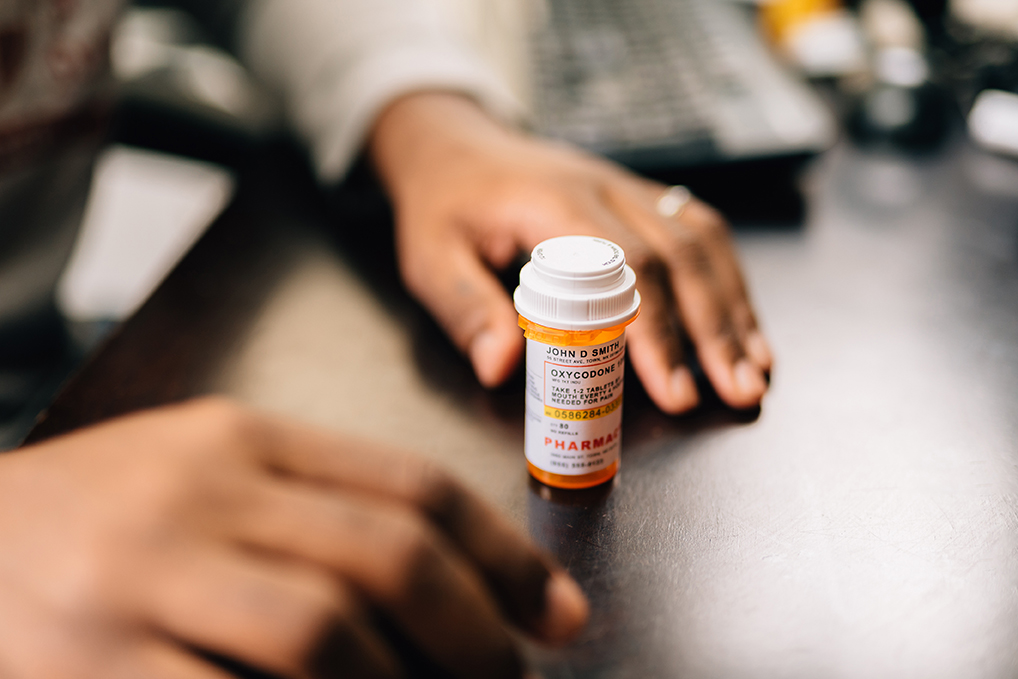 Patient picks up an opioid prescription bottle from a pharmacy counter