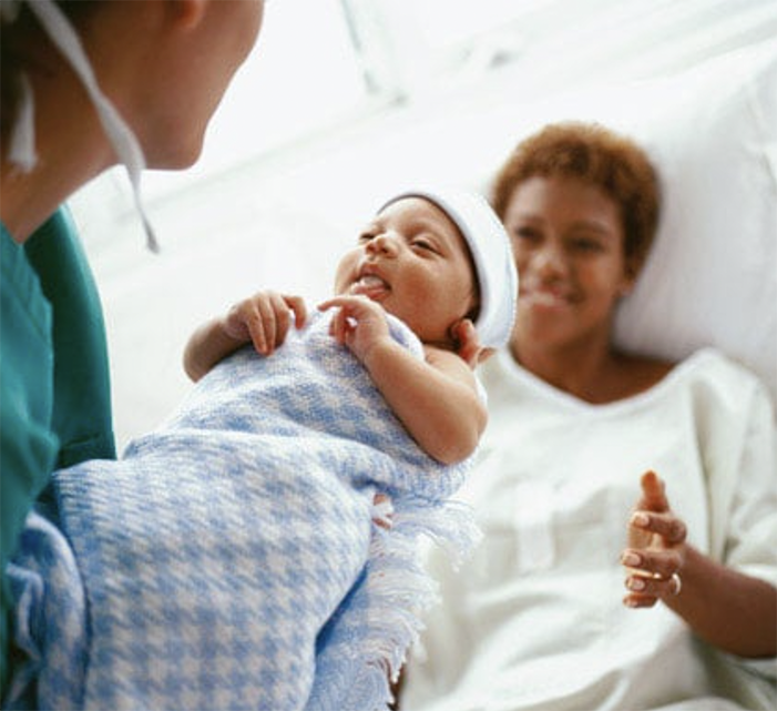 Postpartum nurse holding a new born baby in front of a young mother