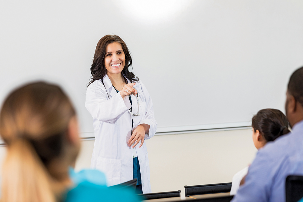 Nurse educator speaking to students in front of a classroom whiteboard