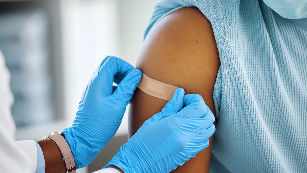 Nurse wearing blue latex gloves applies bandaid to patient's arm after giving vaccine