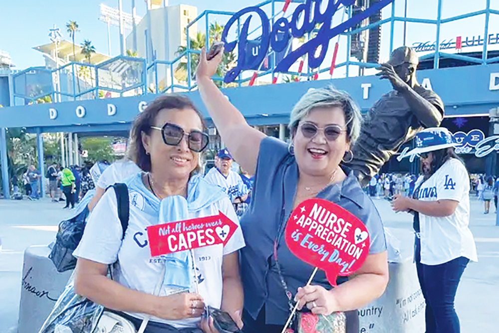 Two nurses wearing t-shirts and carrying signs standing in front of the Dodger Stadium sign.