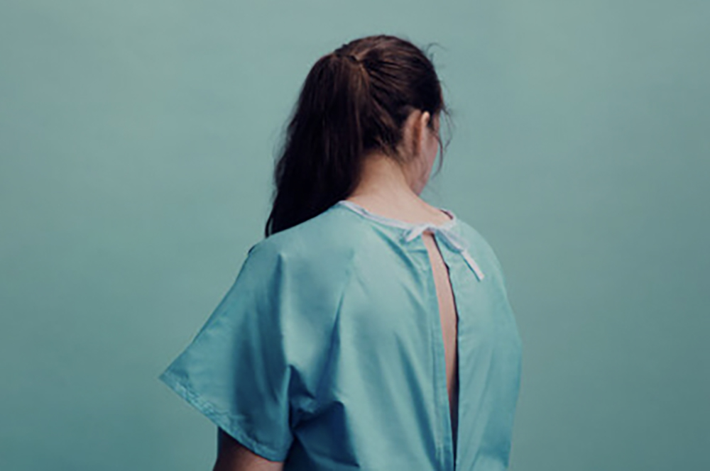 Back view of female patient in surgical gown with her hair over her shoulder.