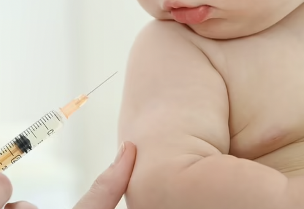 Chubby white infant looks while receiving injection.