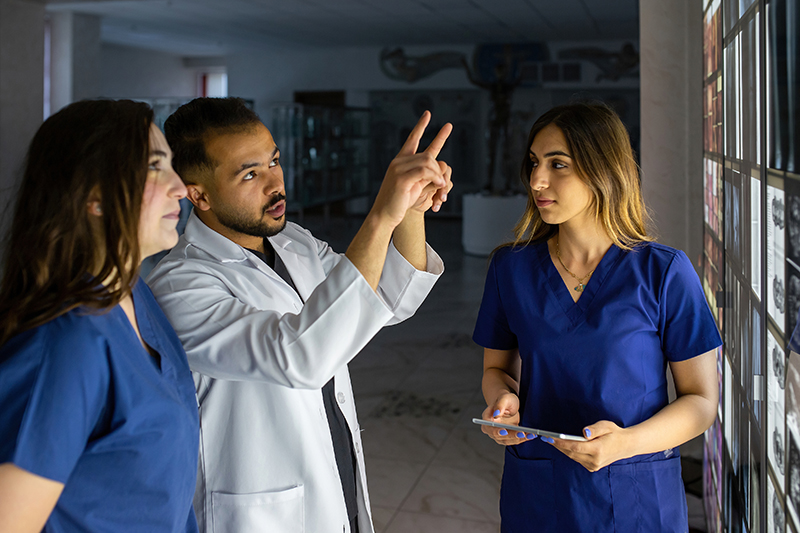 Nursing school professor stands next to two nurses pointing to scans on a lightboard.