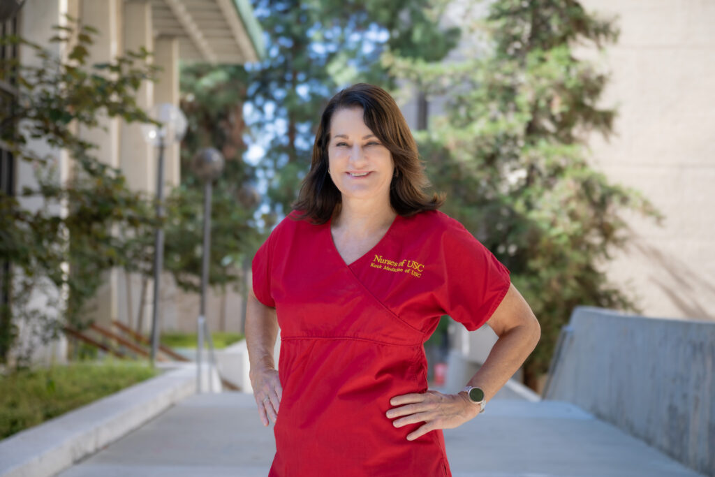 USC Nurse Mary Reed wearing red scrubs and standing outside in front of the USC Ambulatory Care.